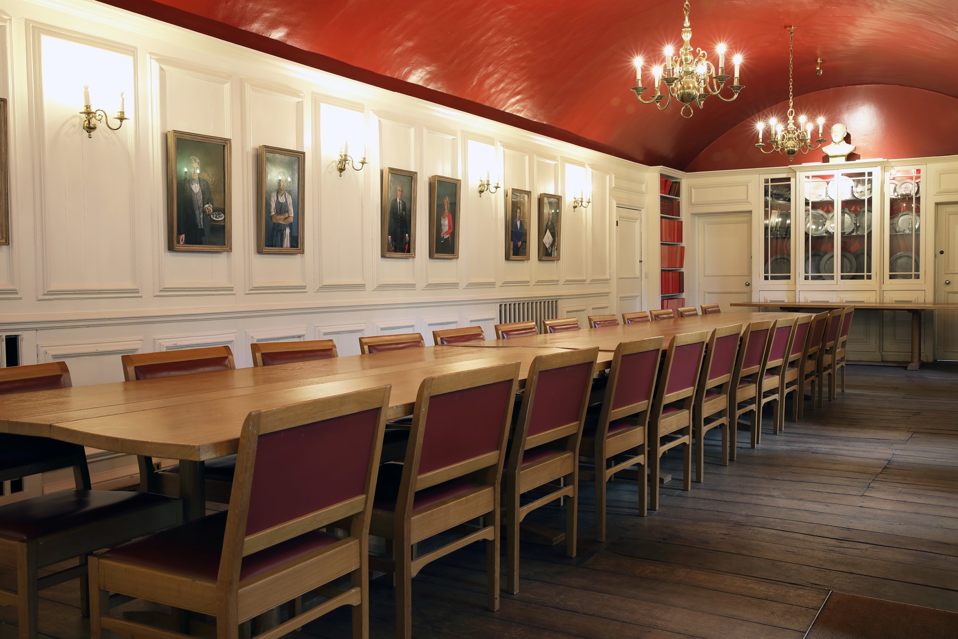The South Undercroft - a room with a red ceiling with a long brown meeting table. Portraits hang on the walls.